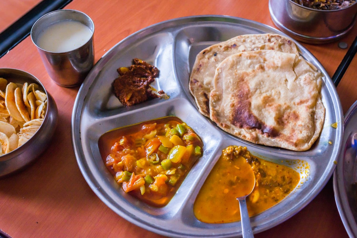 A home-style desi thali: fresh tandoori roti, daal, mixed sabzi and a glass of lassi on a warm wooden table